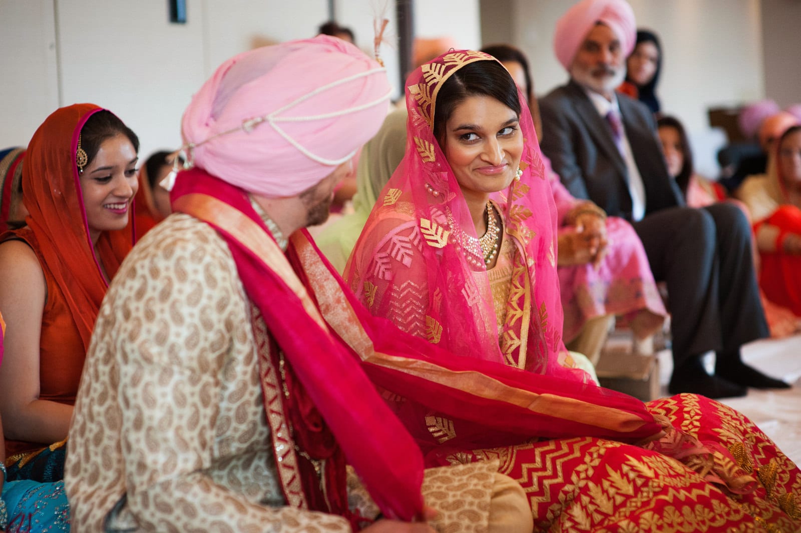 A bride wearing a gold and pink sari looks over at her groom and smiles during their Renaissance Phipps South Asian Wedding.