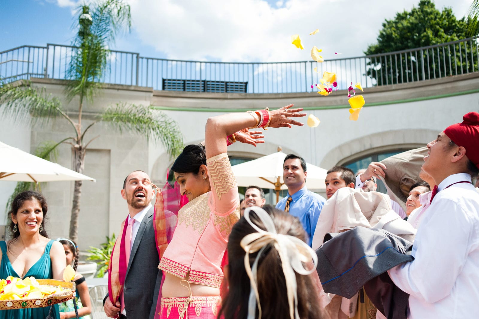 A bride reaches back as she throws flower petals to her guests at the end of her Renaissance Phipps South Asian Wedding.