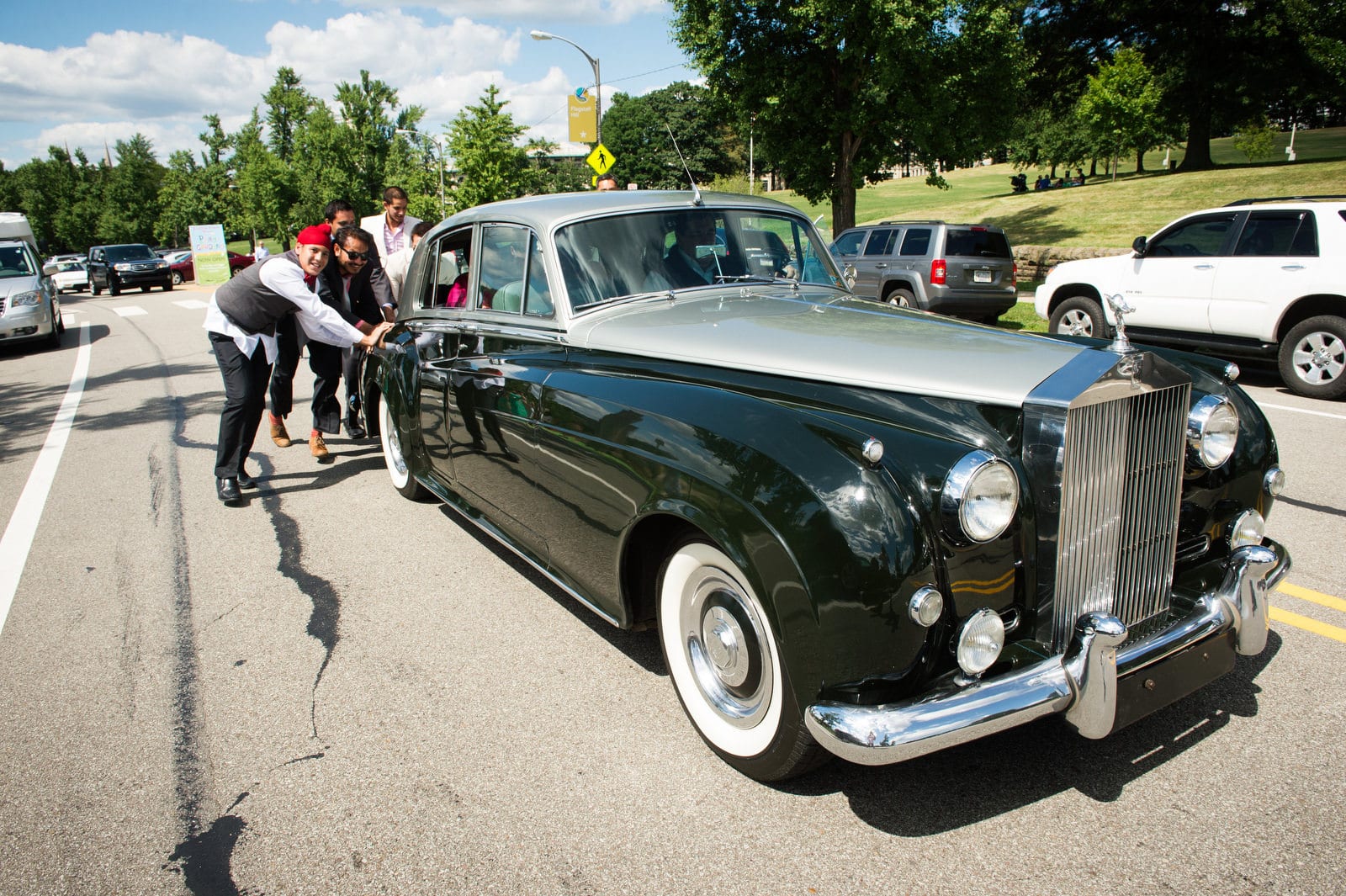 A group of men push a vintage Rolls Royce limousine at the end of a Renaissance Phipps South Asian Wedding.