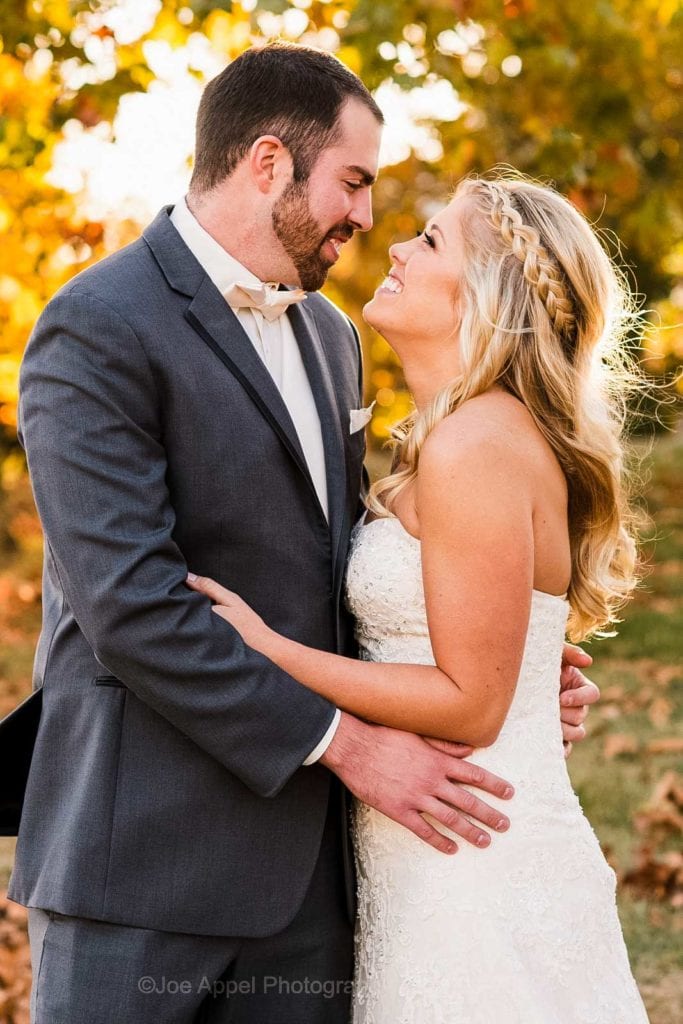 A bride and groom stand in the sunshine and look at each other with golden fall leaves behind them at their Embassy Suites Pittsburgh wedding.