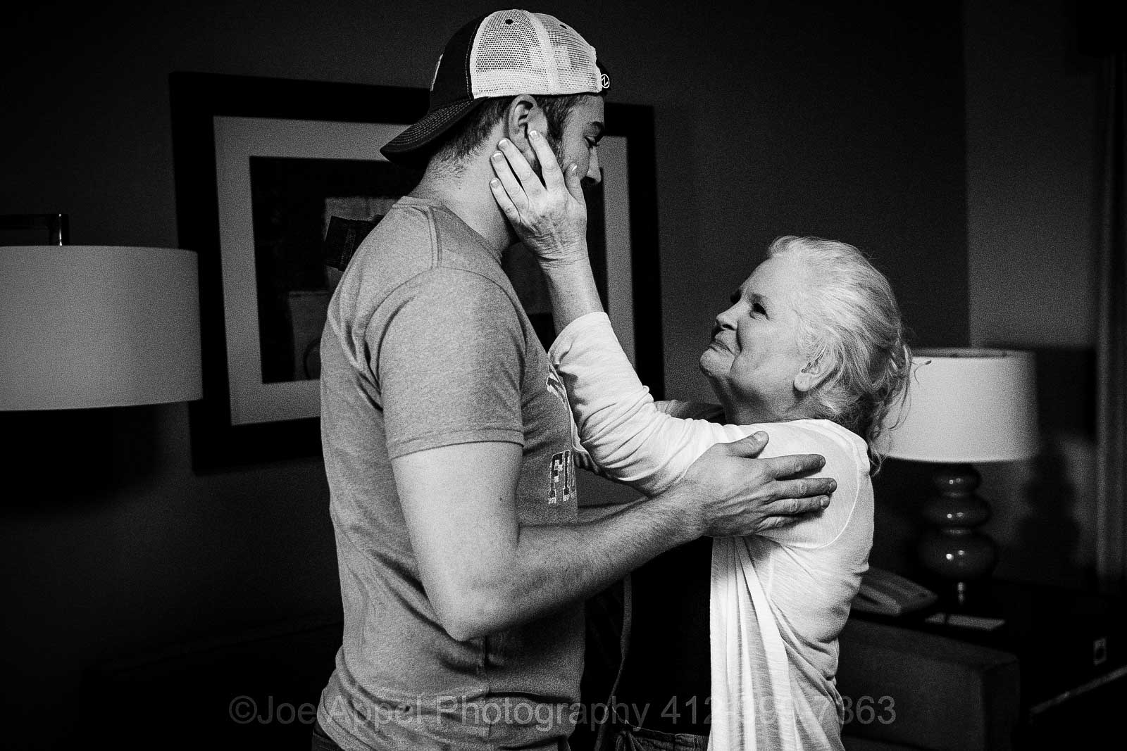 A mother reaches up and touches the cheek of her tall son who is wearing a backwards baseball cap at the Embassy Suites Pittsburgh before his wedding.