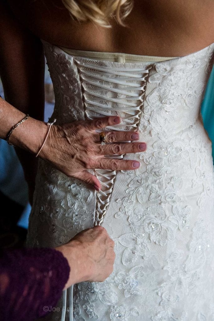 Closeup of a woman's hands as they lace up a brides gown.