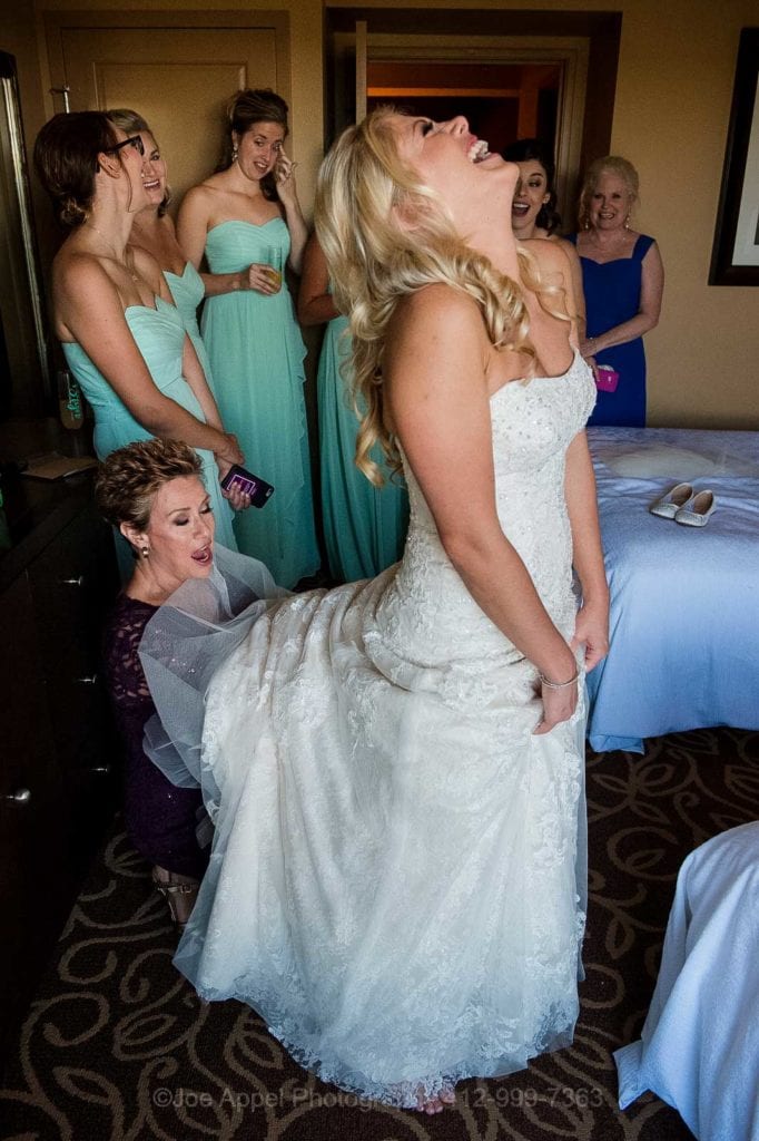 A bride holds back her head and laughs as her mother reaches way up into her dress to adjust her slip before her wedding at the Embassy Suites hotel near Pittsburgh International Airport.