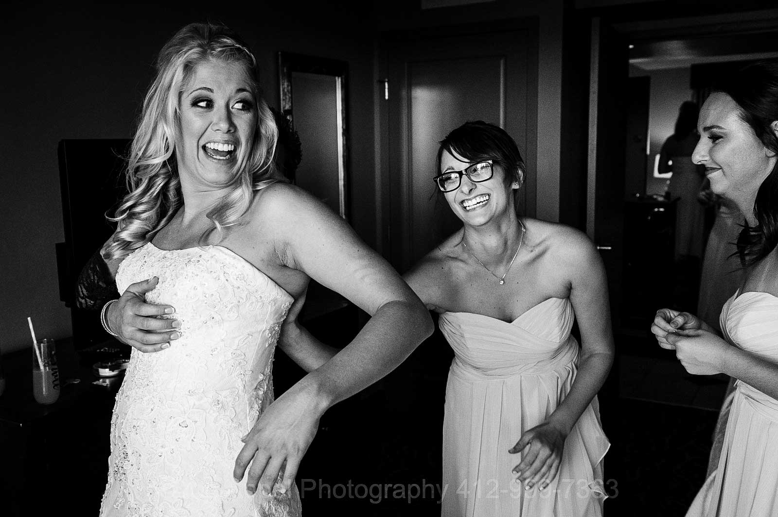 A bride looks back at her bridesmaids and laughs as she gets her wedding dress on.