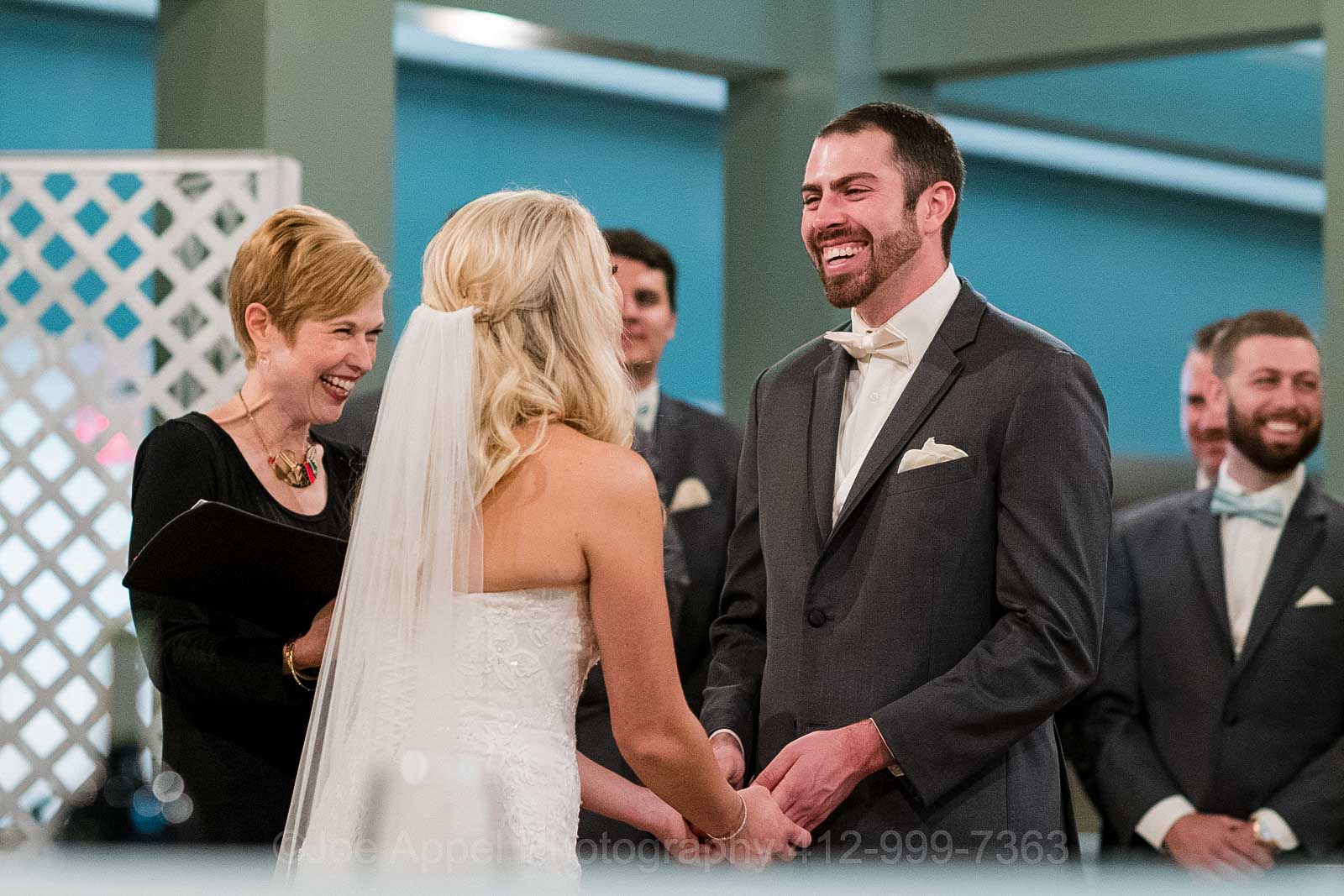 A groom laughs as he holds his bride's hands during their wedding ceremony at the Embassy Suites hotel near Pittsburgh International Airport.