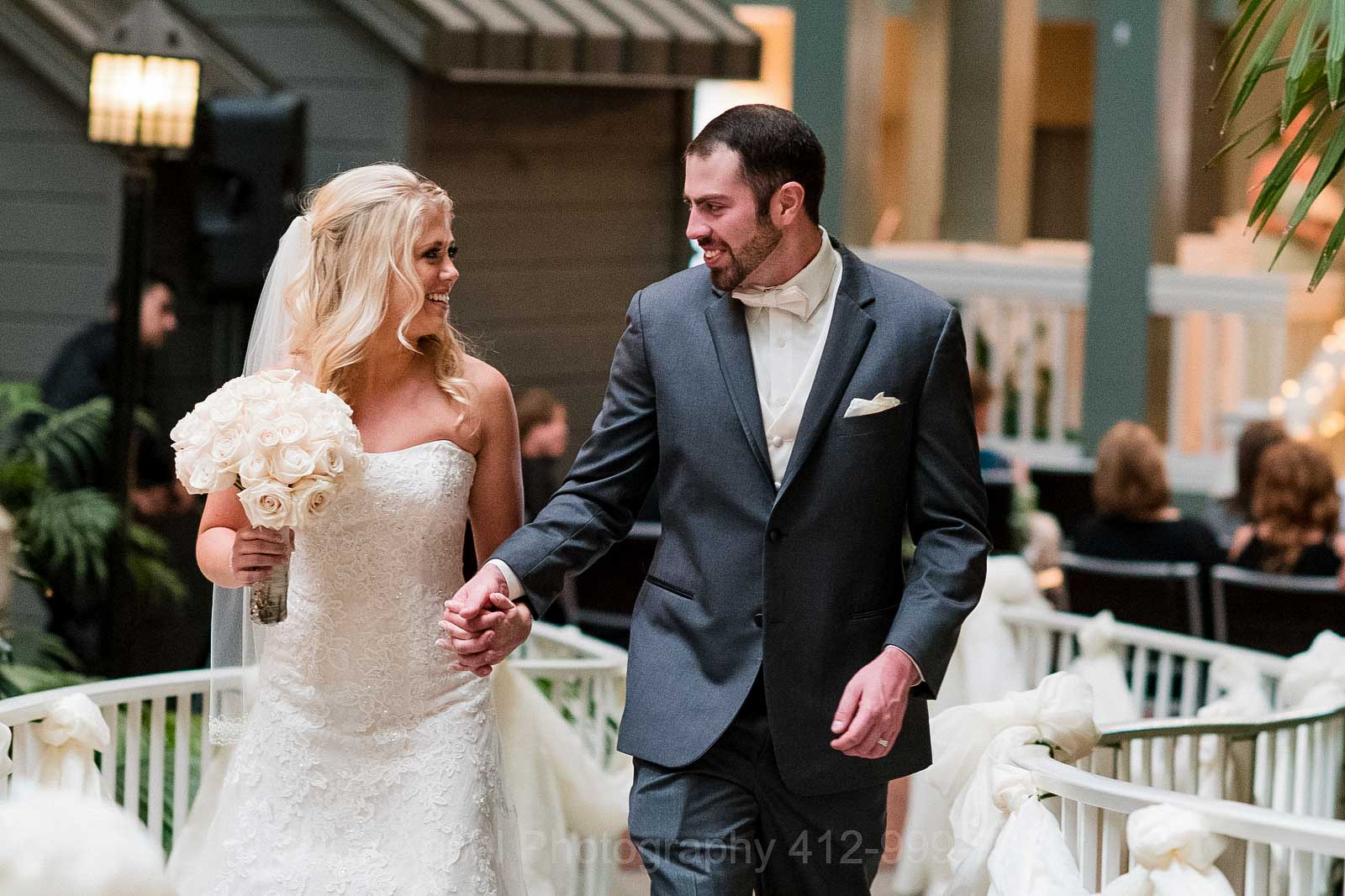 A bride and groom hold hands and smile as they walk along a curved path at the Embassy Suites hotel in Pittsburgh.