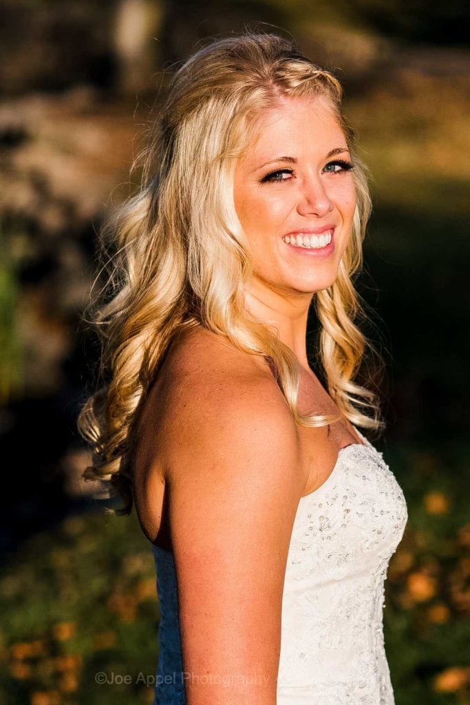 A tan, blonde bride smiles in the sunshine.