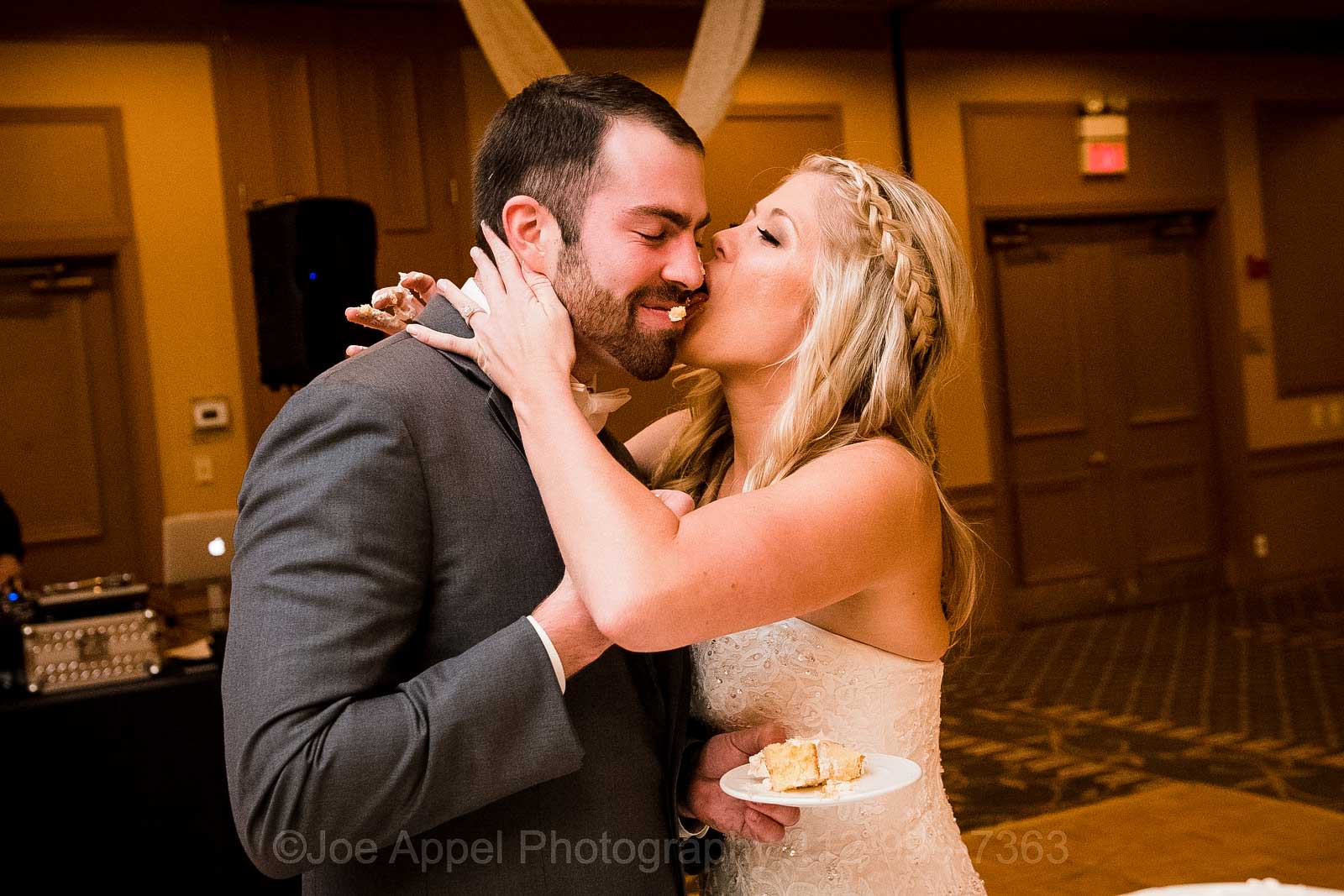 A bride licks her groom's face after smashing cake into it during their Embassy Suites Pittsburgh wedding.