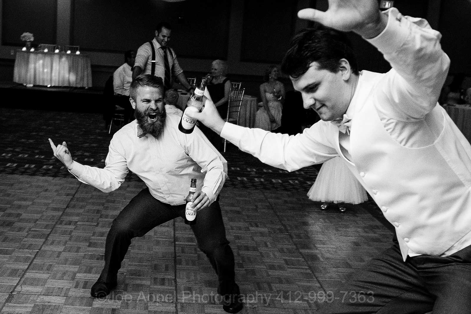 A bearded man yells as another man in a white dress and bow tie dances.