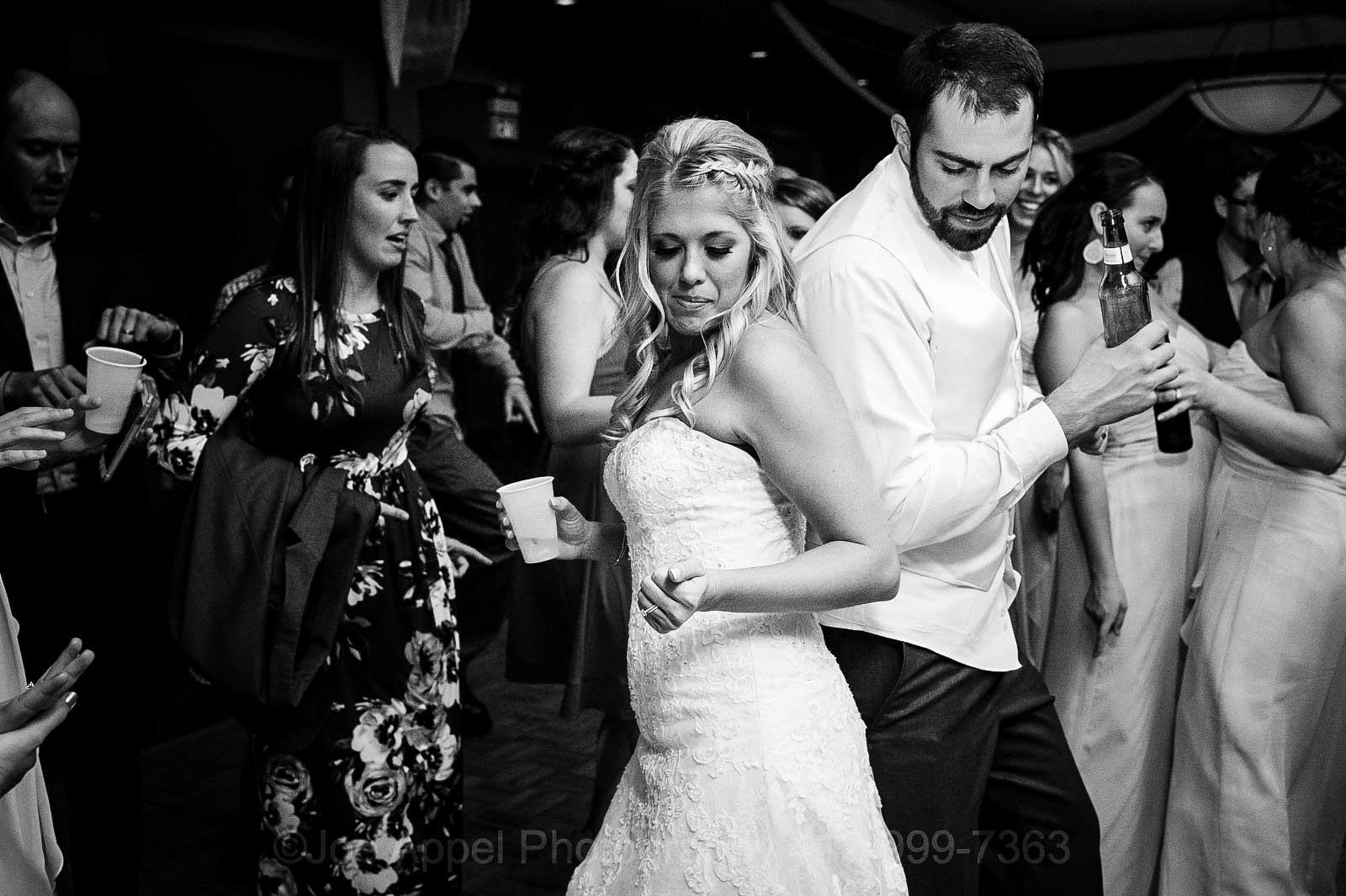 A bride and groom hold drinks as they dance back to back during their Embassy Suites Pittsburgh wedding.