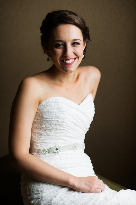 A bride looks at a camera and smiles while wearing a strapless white dress.