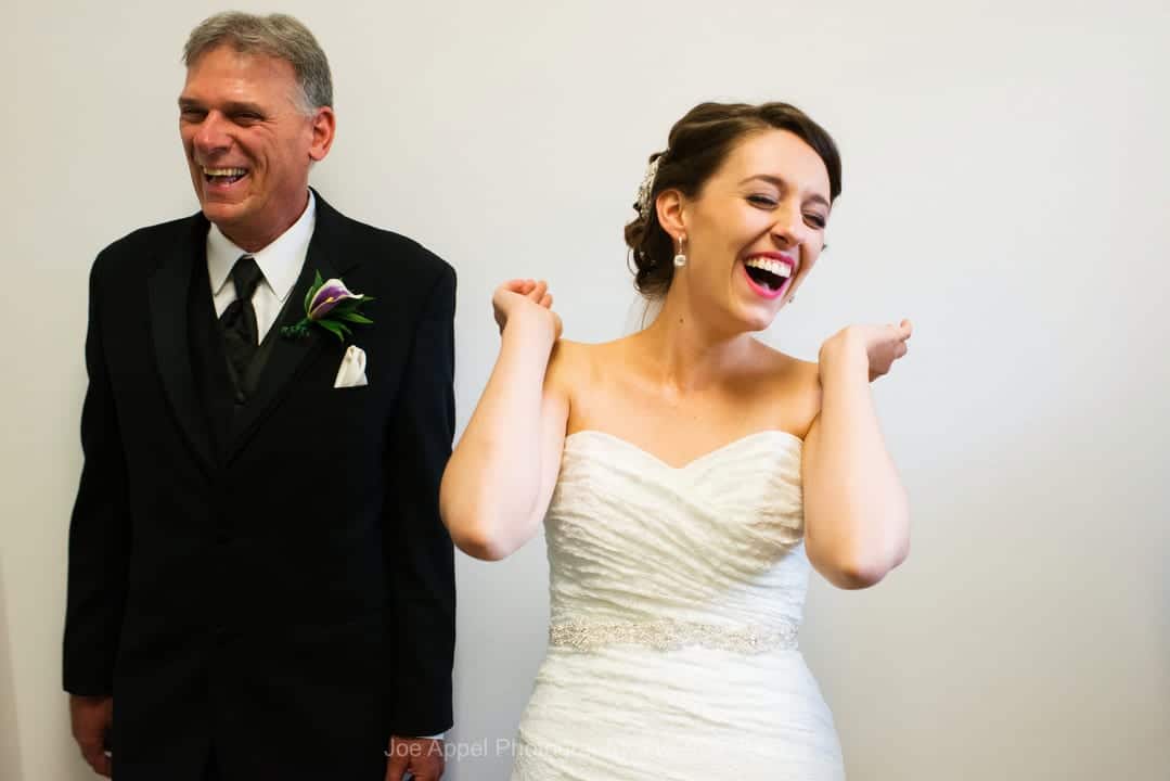 A bride lifts up her hands and laughs while waiting with her father in the back of St. Columbkille for her wedding to begin.