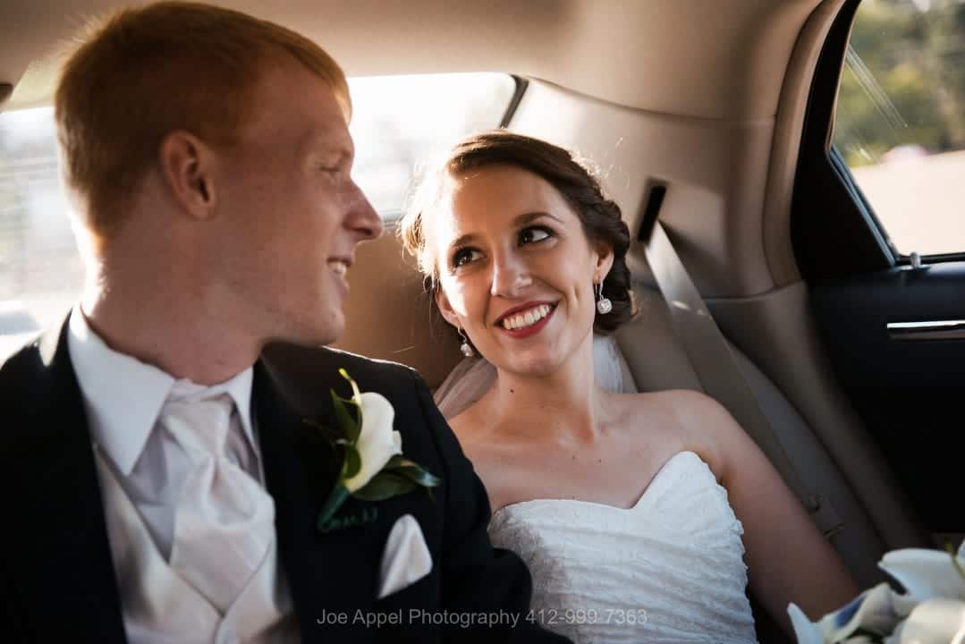 A bride smiles at her groom while in the back seat of a limousine.