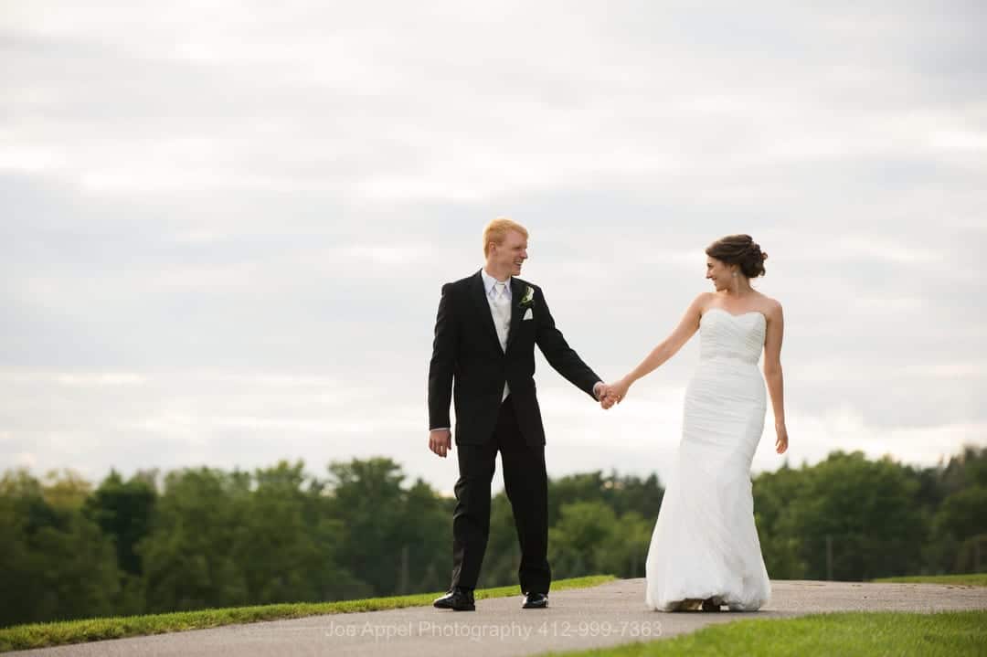 A bride and groom hold hands while walking on a path before their Montour Heights Country Club wedding.