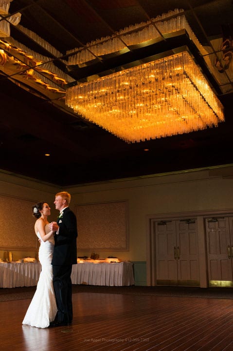 A bride and groom dance beneath a warm-toned chandelier during their Montour Heights Country Club wedding