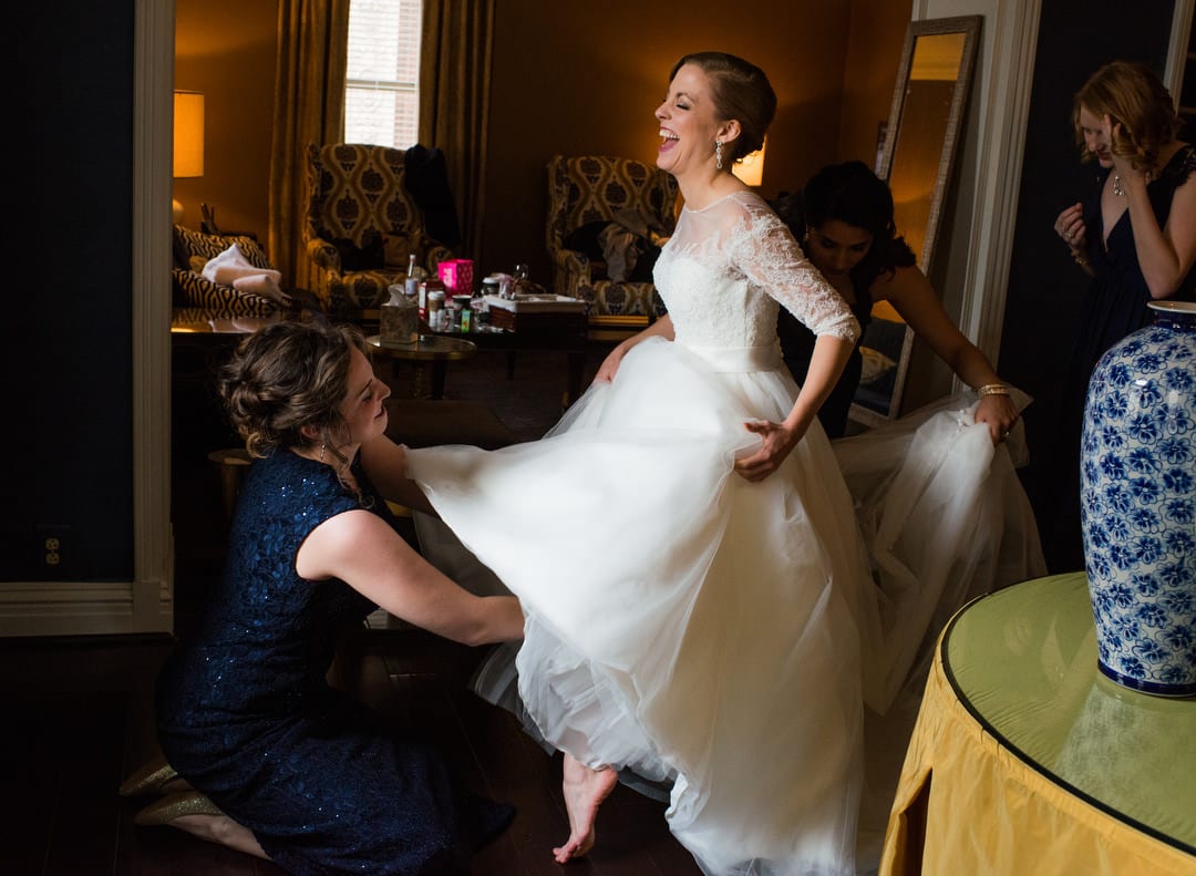 A bride laughs as a bridesmaid reaches up under her dress to adjust her garter belt at the William Penn hotel in Pittsburgh.