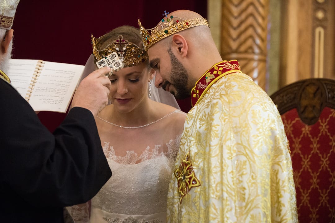 A priest blesses a crowned bride and groom as they stand on the altar of St. Mary's Coptic Orthodox church in Ambridge.