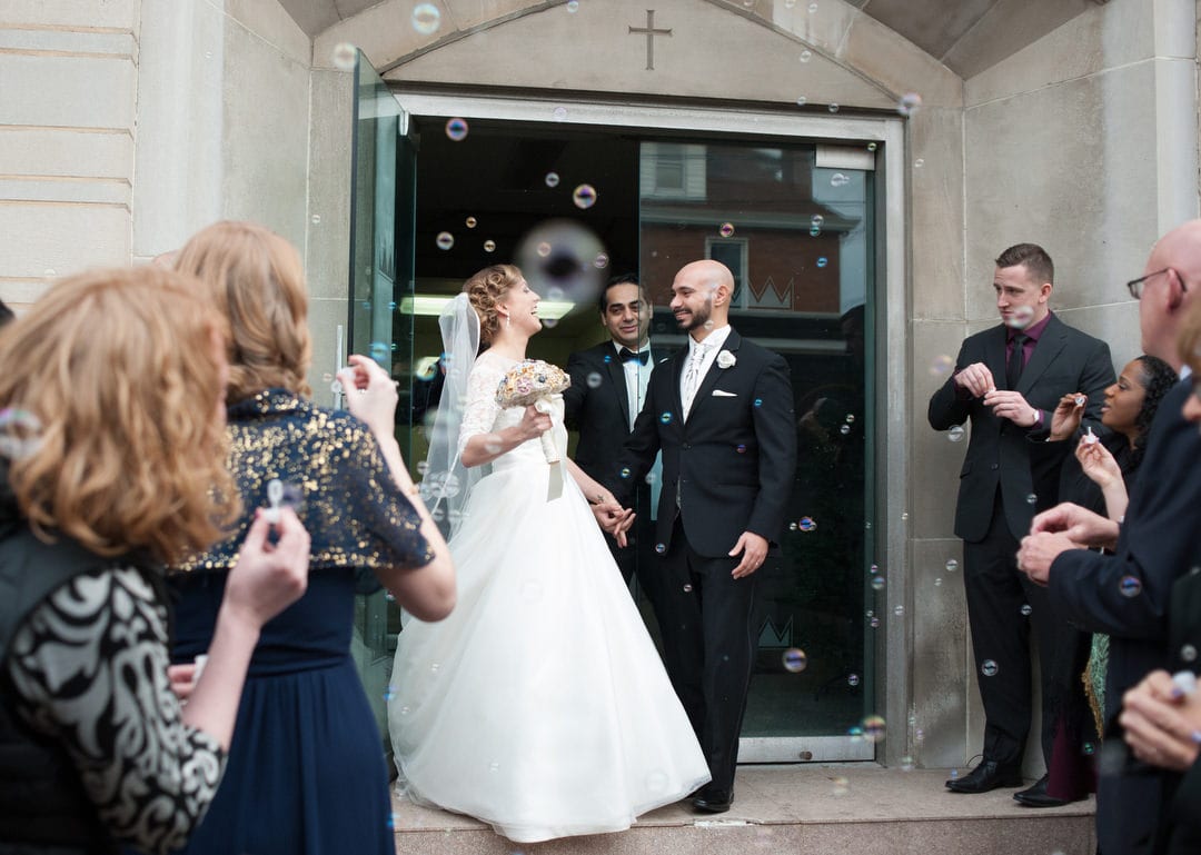 A bride and groom exit St. Mary Coptic Orthodox church to guests blowing bubbles.