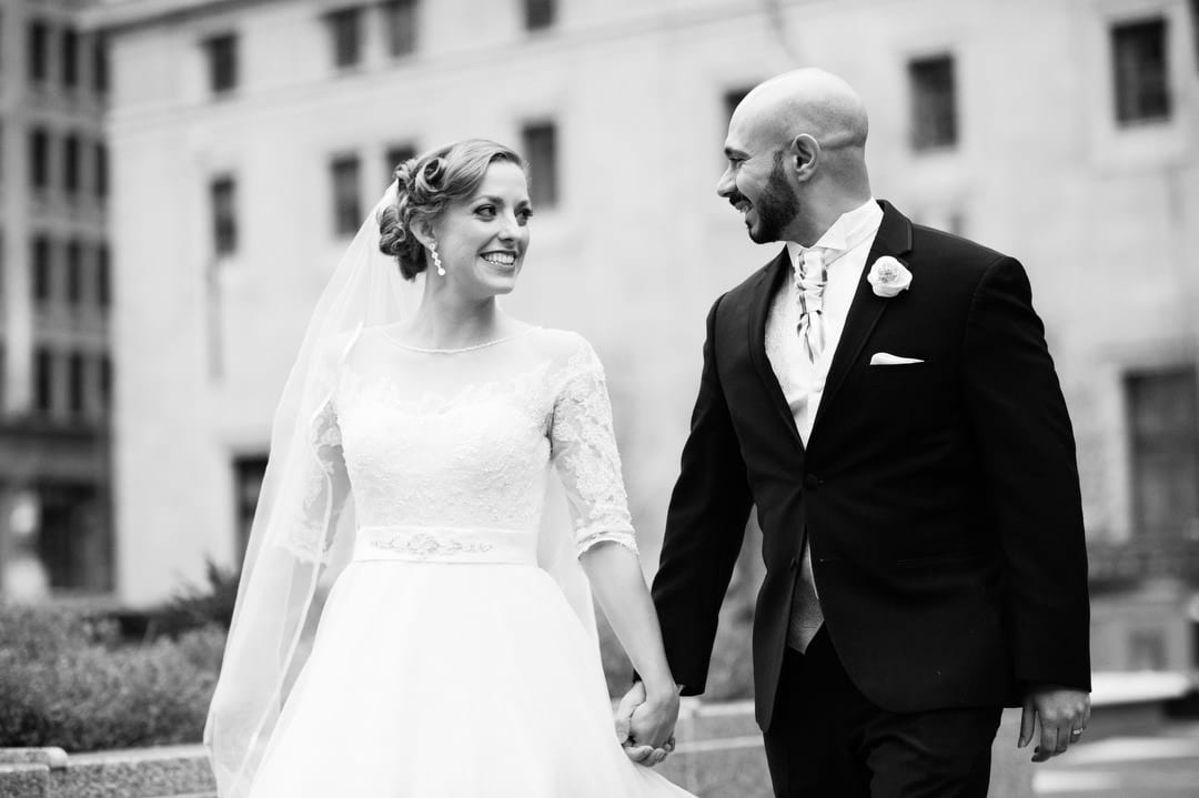A bride and groom smile and hold hands in Mellon Square Park during their Coptic wedding at the William Penn.