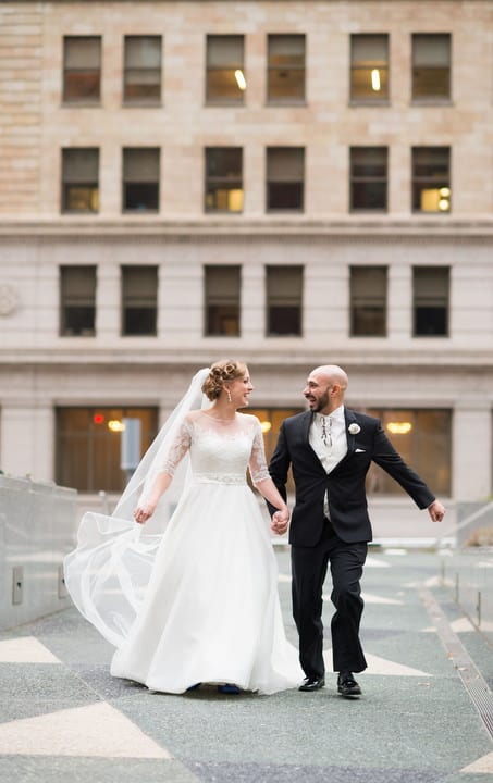 A bride and groom hold hands and smile as they run through Mellon Square park in Pittsburgh.