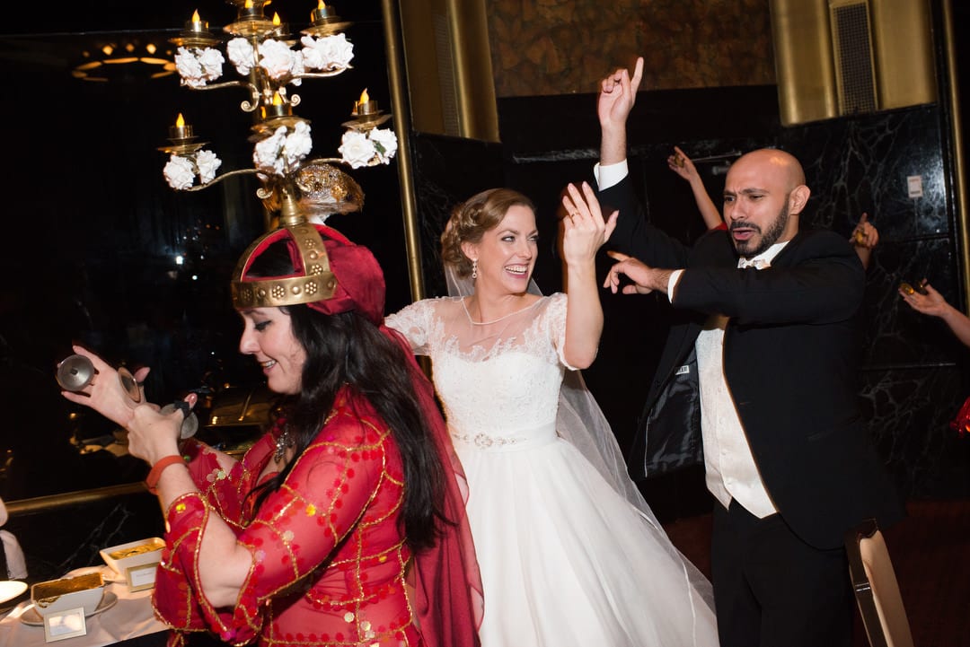 A bride and groom dance in a procession led by a woman in a red dress with a large lamp on her head during their Coptic wedding at the William Penn.