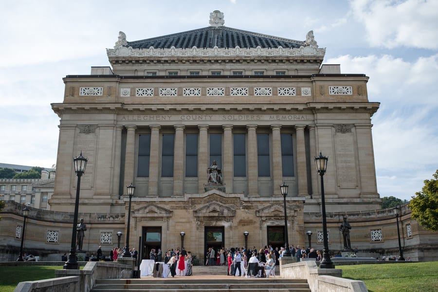 People stand around the front steps of Soldiers and Sailors Memorial Hall during a cocktail hour of a wedding reception.