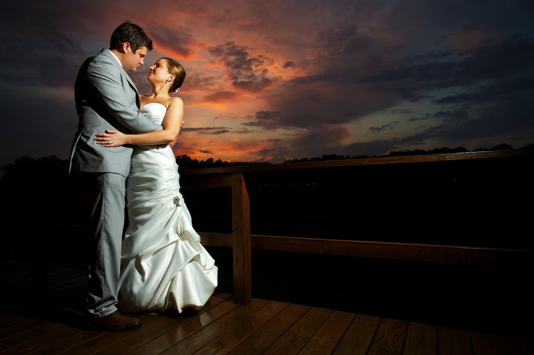 A bride and groom hold each other in front of a dramatic sunset.
