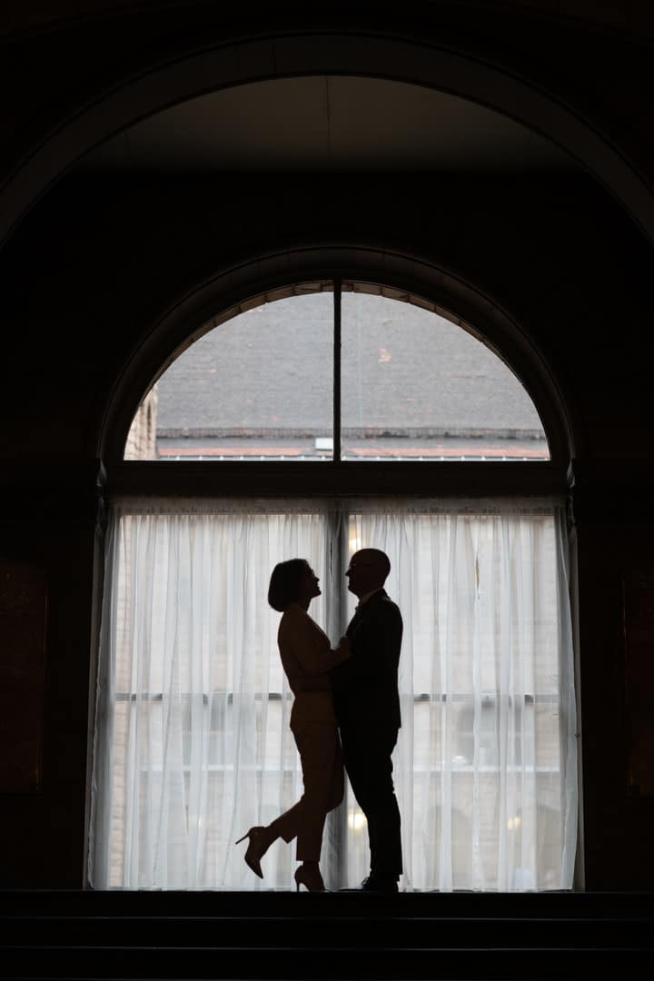 A man and a woman are silhouetted in the arched window at the top of the stairs at the Allegheny County Courthouse.
