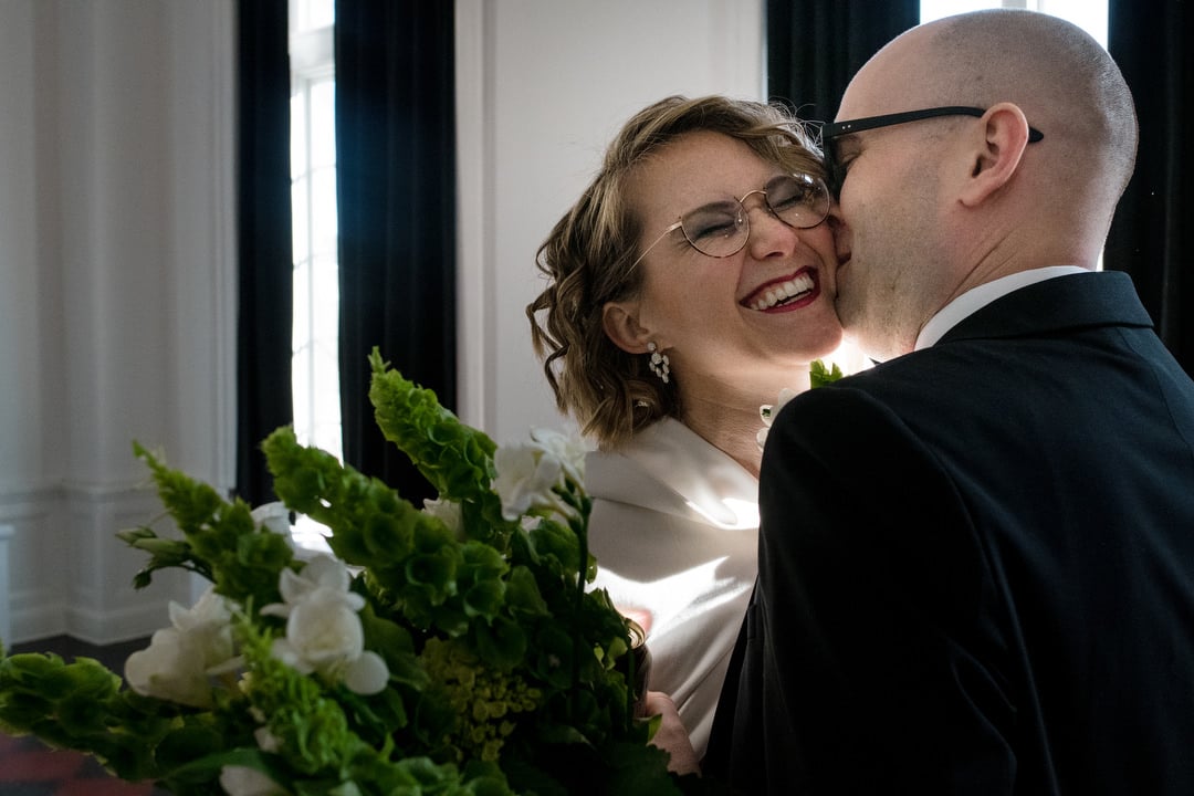 A grinning bride is kissed on the cheek by her groom at their Ace Hotel wedding.
