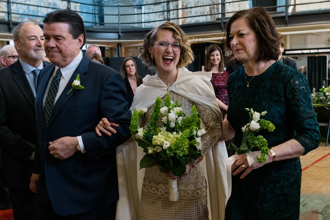 A laughing bride walks with her mother and father into the gym during her Ace Hotel wedding.