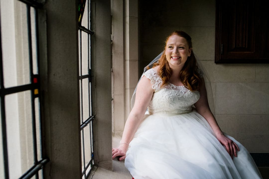 A red haired bride sits on the window sill in the back of Sacred Heart Church in Shadyside Pittsburgh.