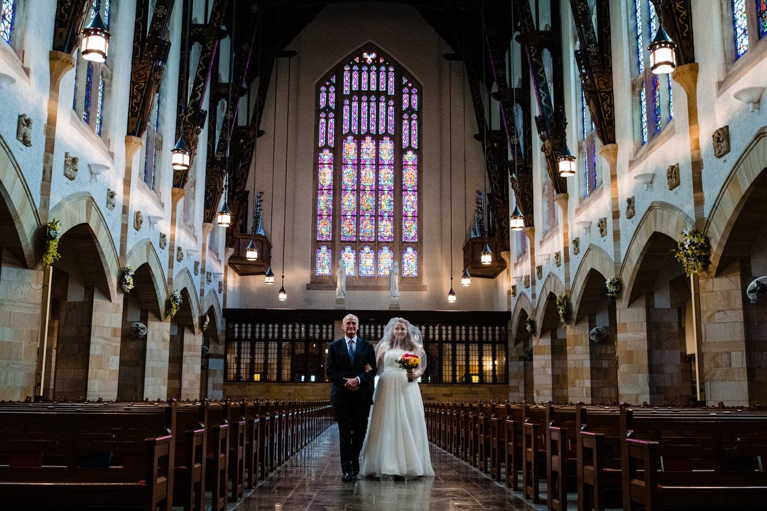 A bride and her father walk down the aisle inside of an empty Sacred Heart Church in Pittsburgh