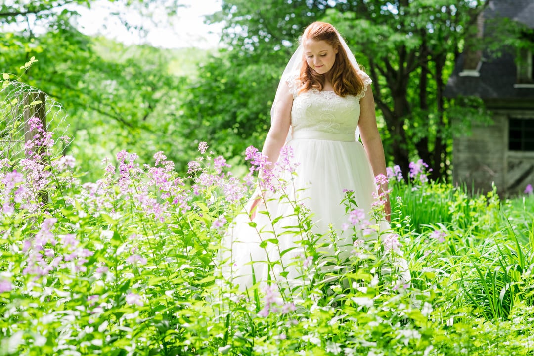 A bride stand in a sunny field of purple flowers.