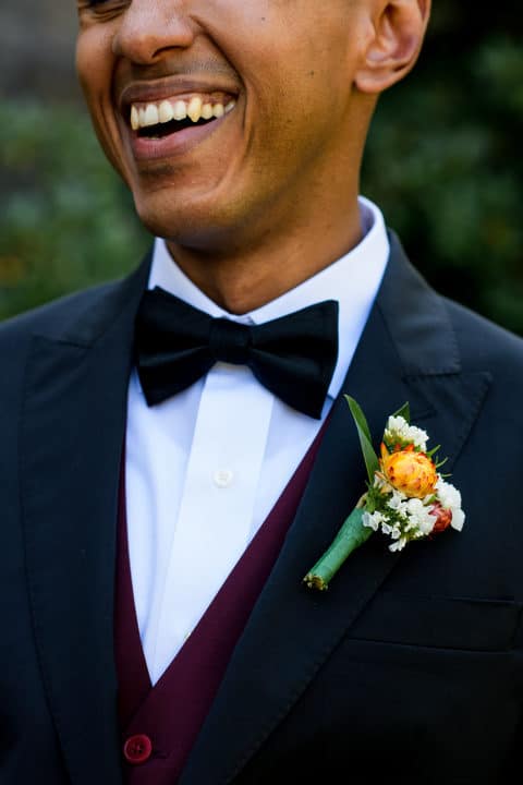 Detail of a boutonniere on the lapel of a groom's dark suit. The flowers are white, green and orange. 