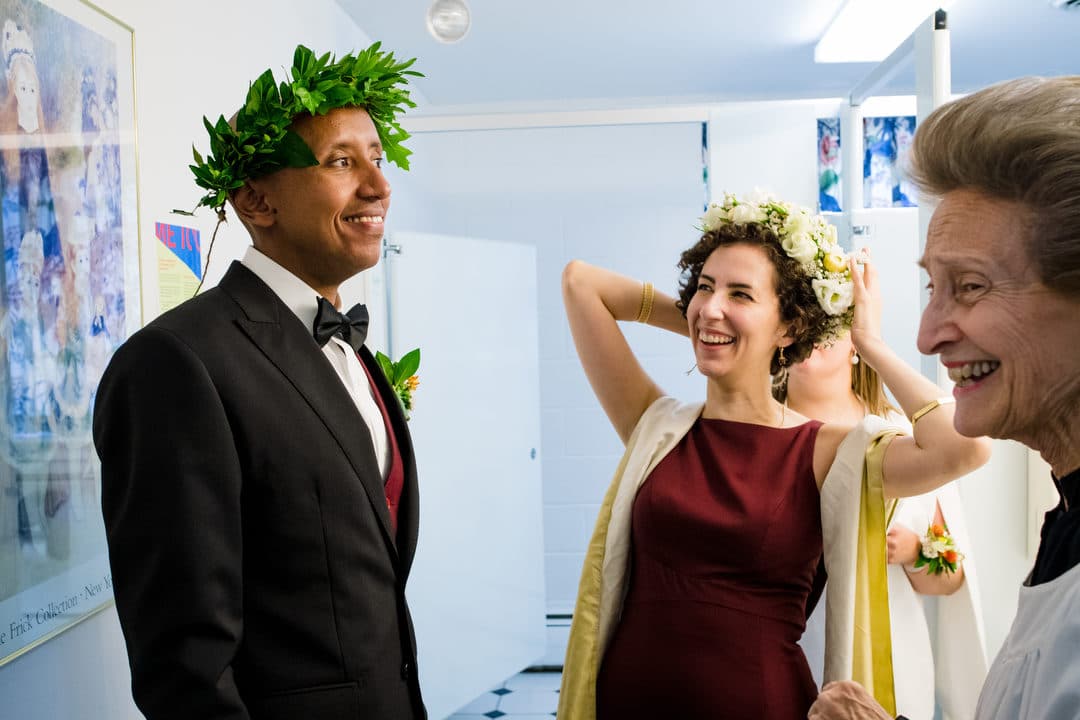 A bride and groom smile as they put on flower and oakleaf crowns before their wedding.