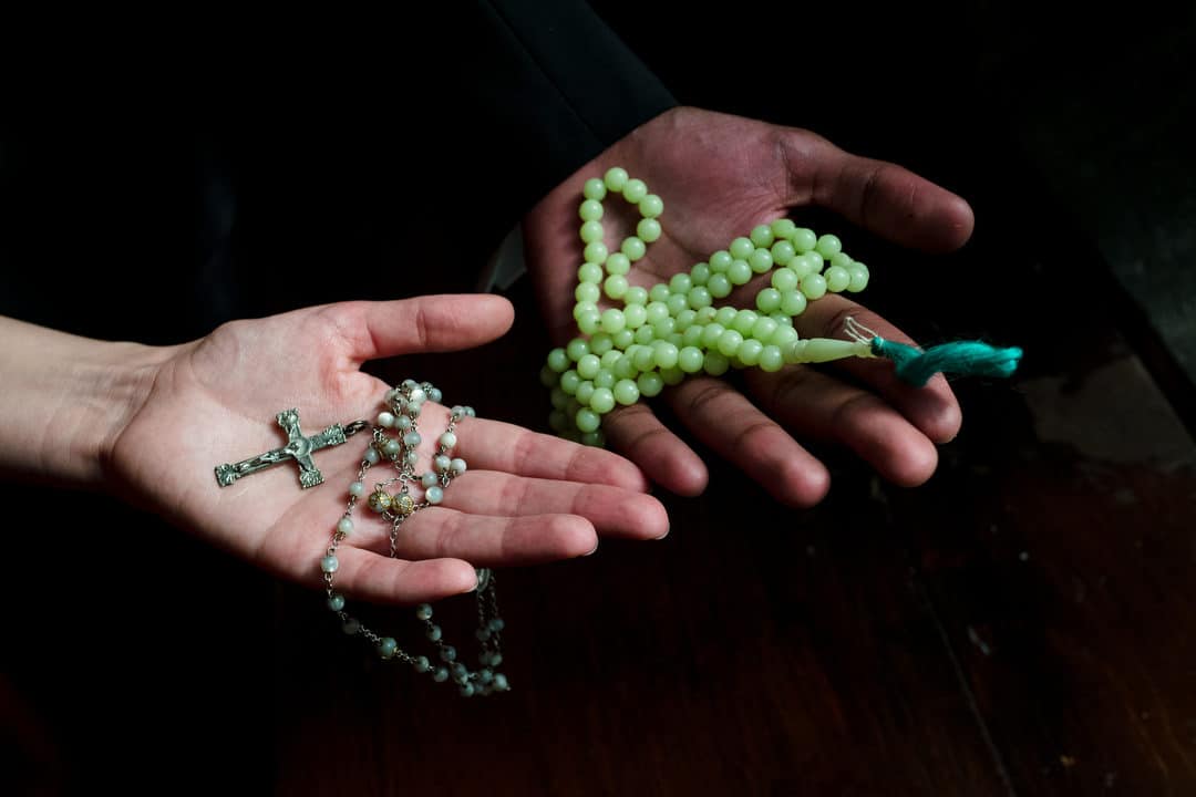 Detail of a bride's hand and a groom's hand. Each hold a rosary.