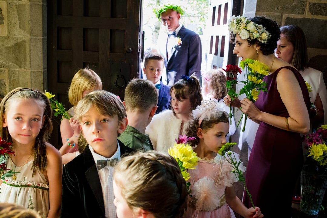 A bride hands flowers out to a group of children gathered before her wedding procession.