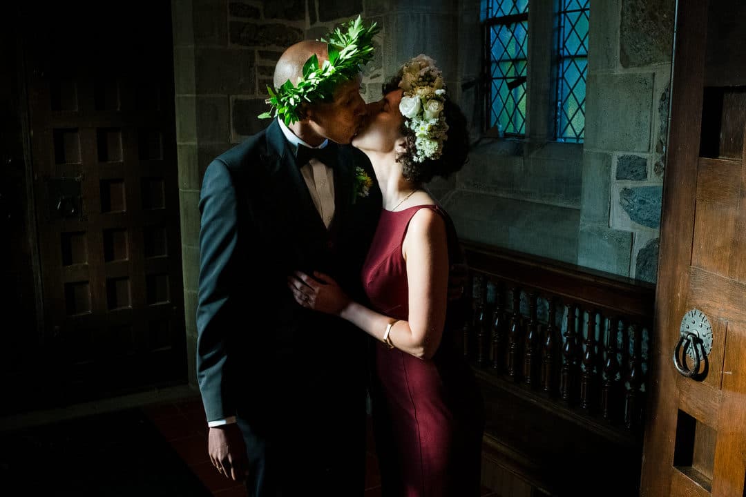 A couple wearing flower crowns kisses in the back of the church during a moment alone just after their wedding ceremony.