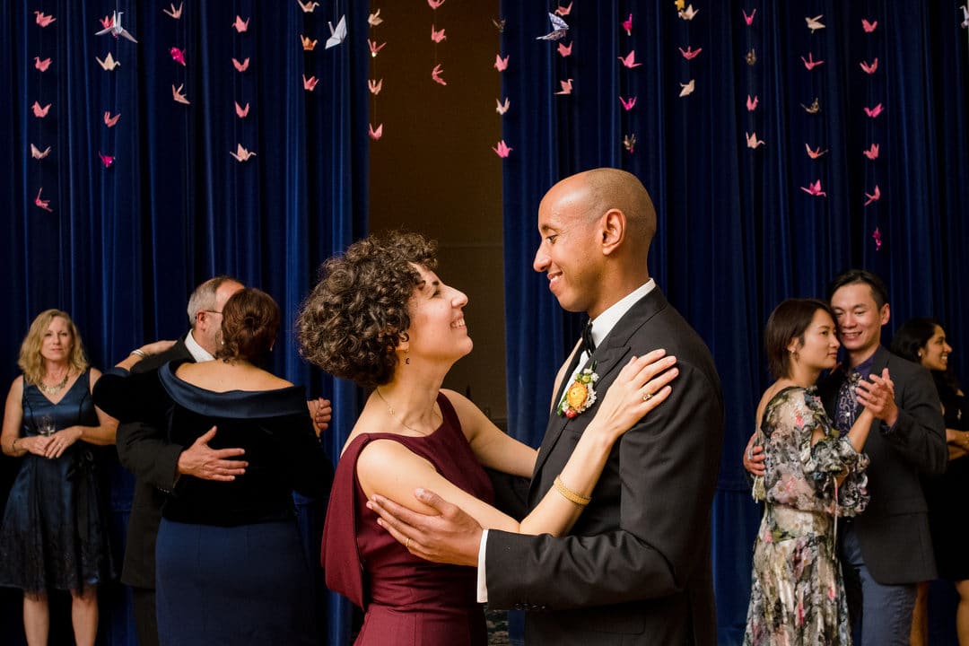 A bride and groom slow dance in front of dark blue curtains during their wedding reception.