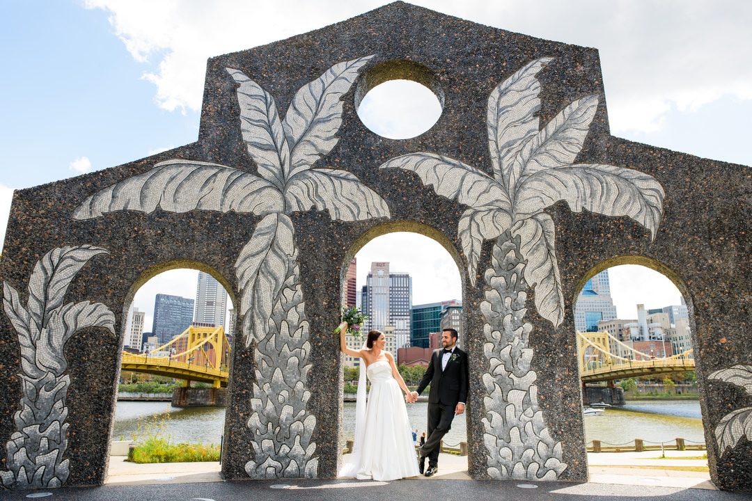 A bride and groom stand beneath a sculpture with palm trees emblazoned on it.