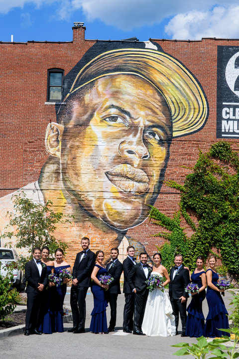A bridal party stands in front of a large mural of Roberto Clemente.