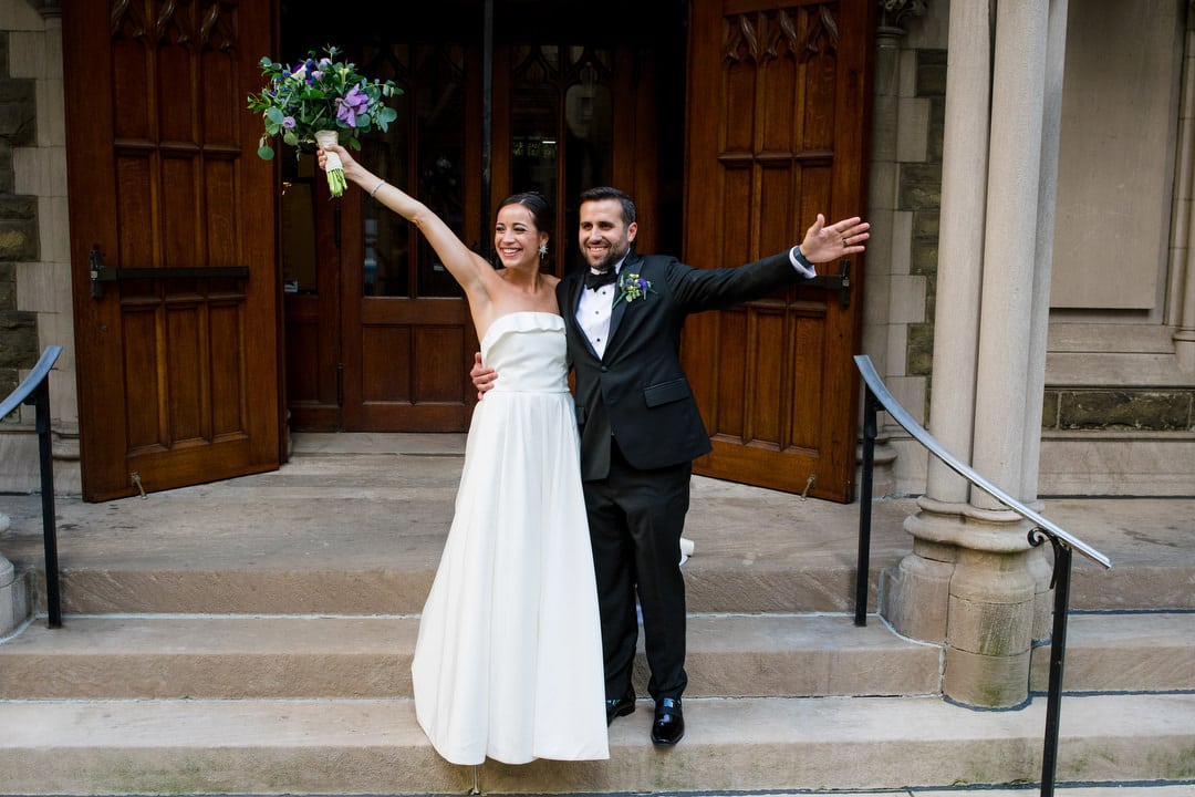 A bride and groom hold their arms outstretched as they wave to guests after their wedding at the First Presbyterian Church in Pittsburgh.