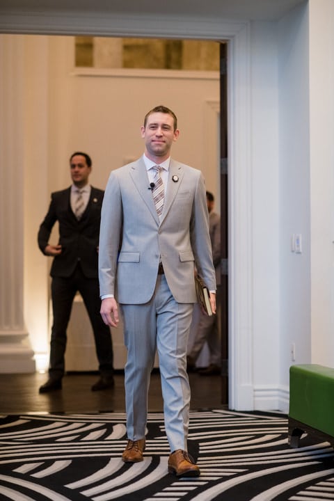 A groom wearing a gray suit and brown shoes walks in to the Sophia ballroom at the Hotel Monaco before his winter wedding.