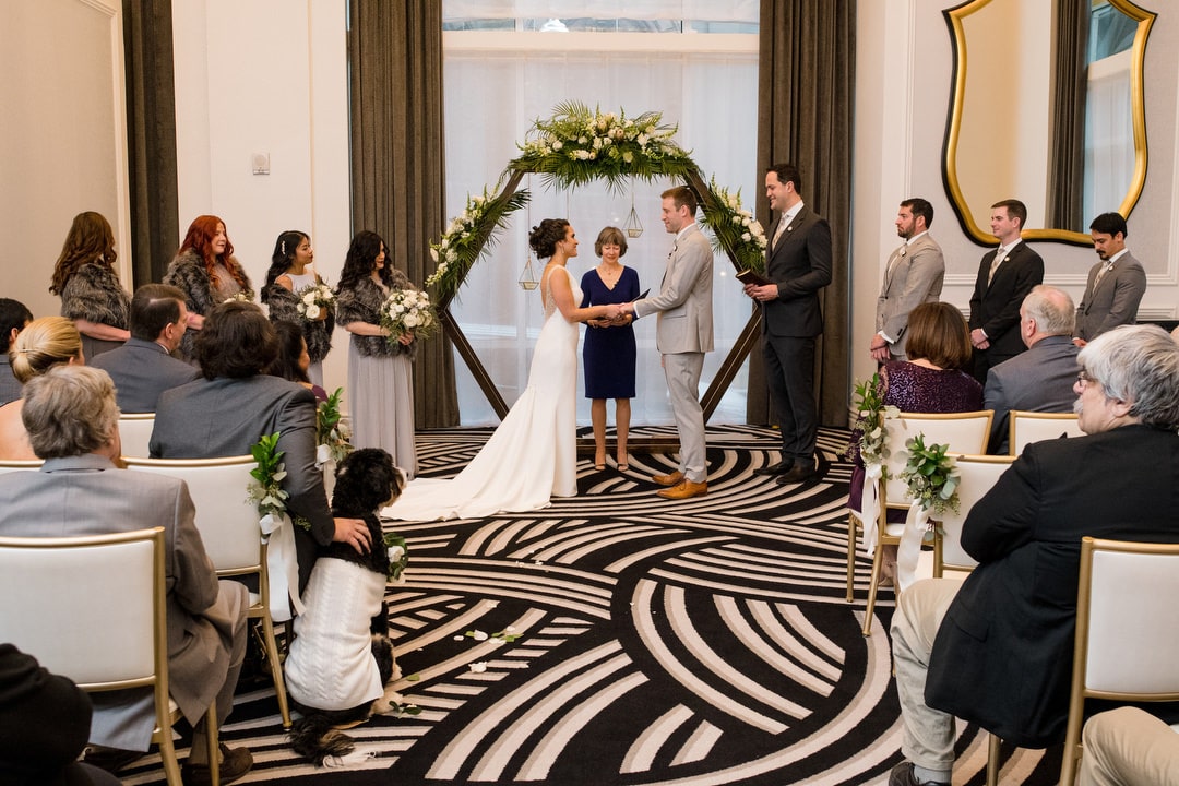 A bride and groom stand in front of a hexagon arch while holding hands during their wedding ceremony at the Hotel Monaco in Pittsburgh.