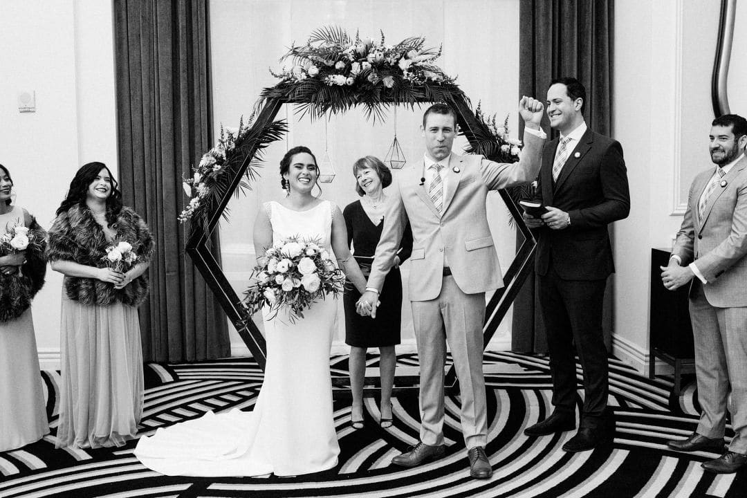 A bride smiles as her groom raises his fist in the air at the end of their wedding ceremony at the Hotel Monaco in Pittsburgh.
