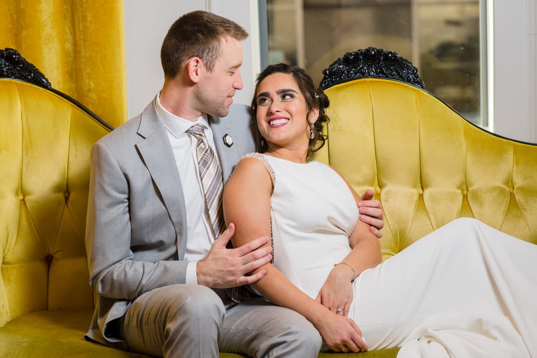 A bride and groom sit together on the yellow couch at the Hotel Monaco in Pittsburgh.