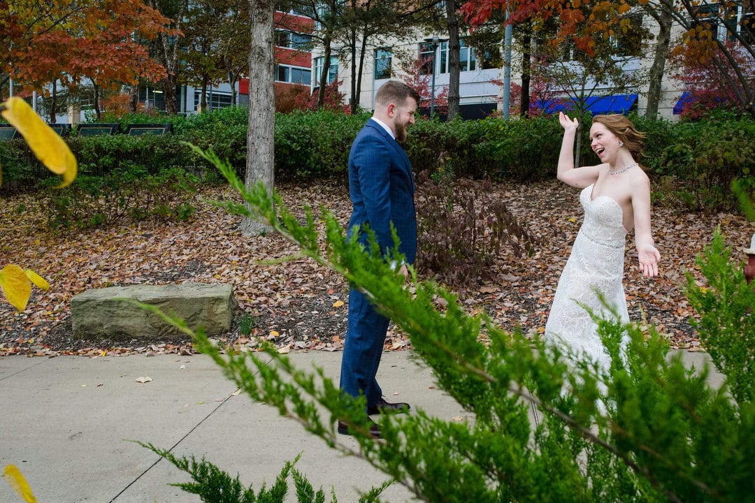 A bride holds her hands out and smiles as her groom gets a look at her before their Pittsburgh Aviary wedding.
