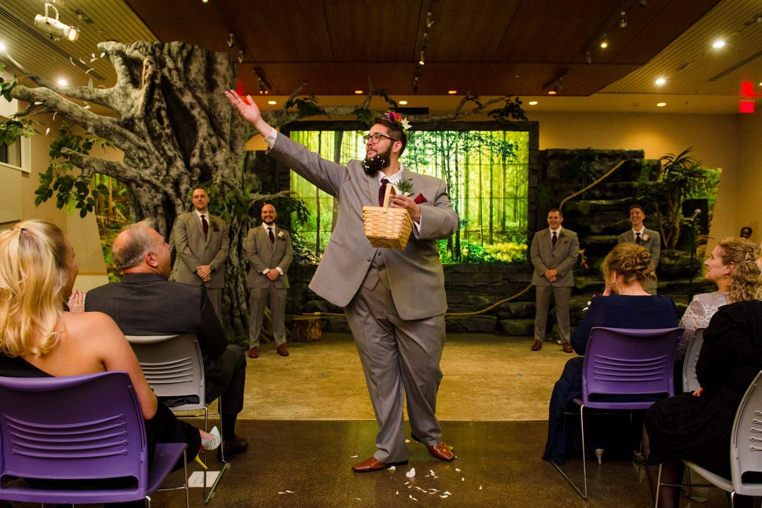 A man with flowers in his beard tosses flower petals as he acts as a flower girl during a Pittsburgh Aviary wedding.