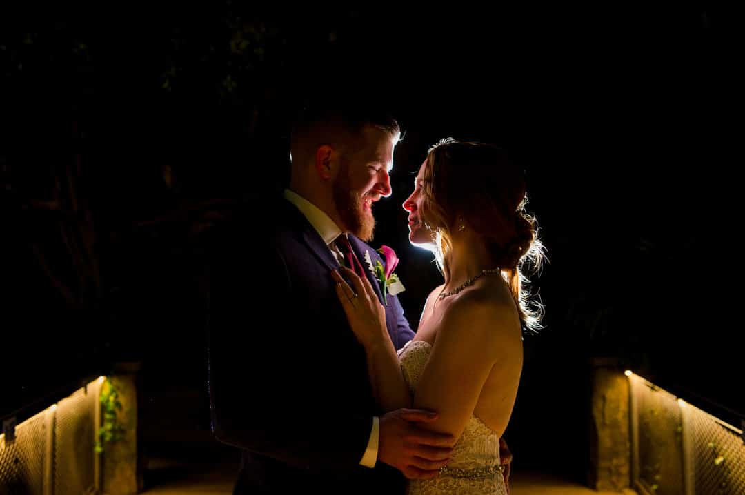 A bride and groom stand in the dark and smile at each other as they're lit from behind at their Pittsburgh Aviary wedding.