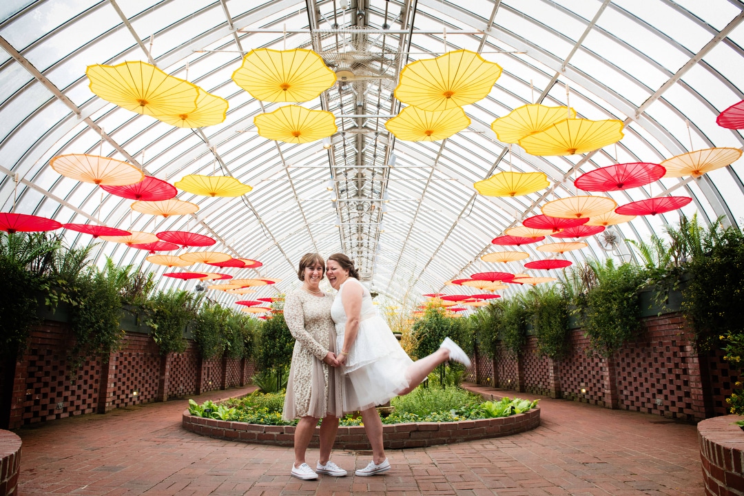 A same sex couple pose for portraits while wearing white dresses and sneakers before their small wedding at Phipps.
